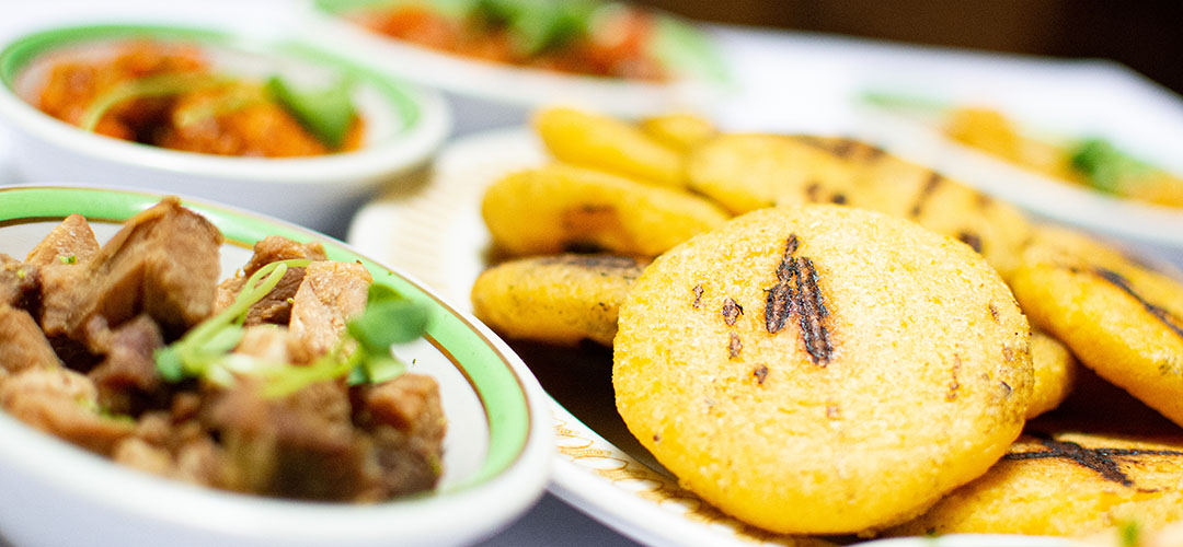 Arepas de maíz, acompañadas de carne y diferentes platos servidos sobre una mesa.
